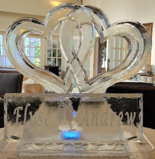 Clear ice sculpture of two intertwined hearts on a black base with a glowing blue light beneath it