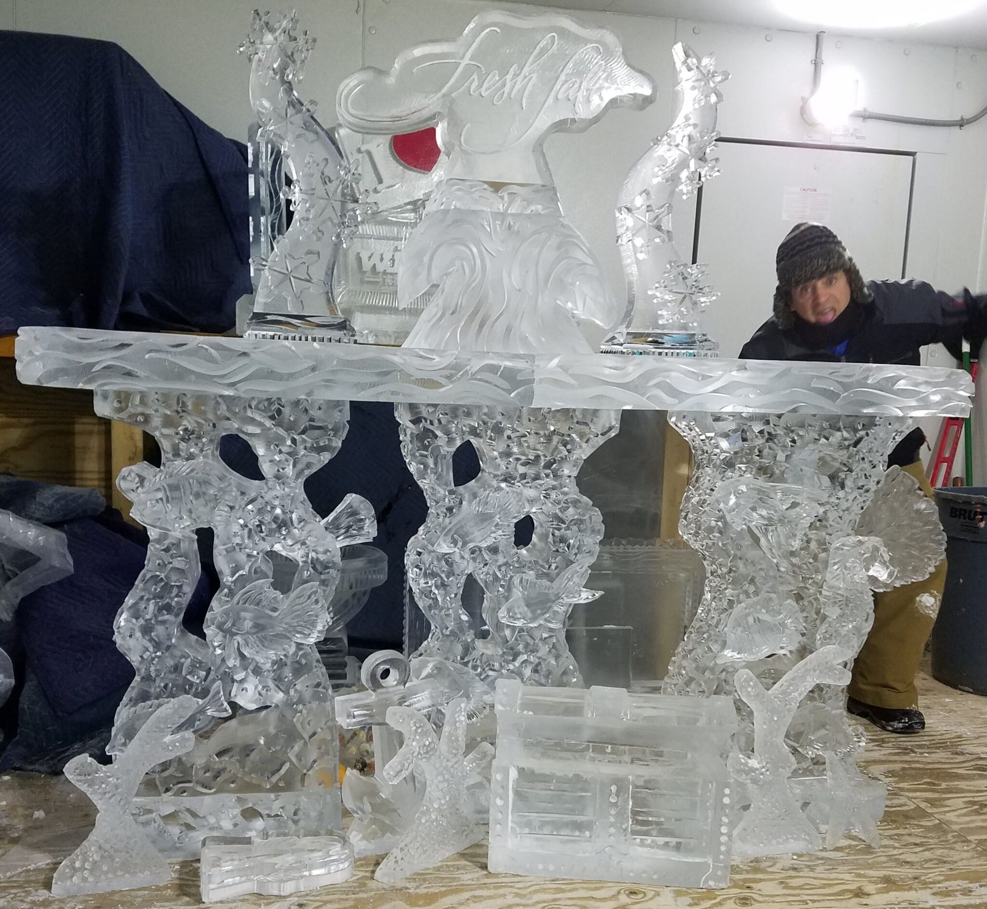 Clear ice sculpture display in an indoor workshop, with a person in dark clothing standing beside it.