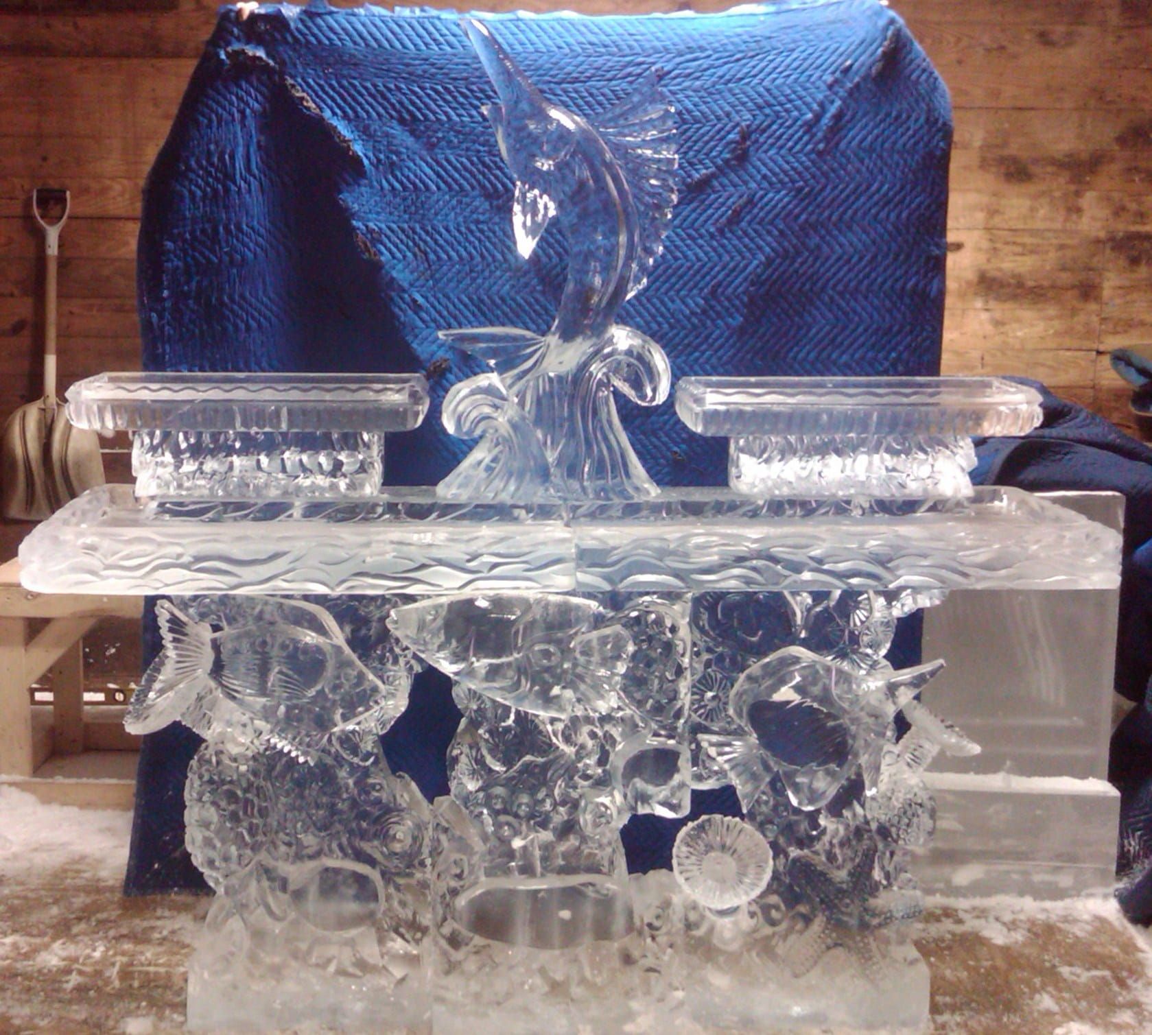 Transparent glass sculpture with blue foil backdrop and clear glass bowls on a reflective base.