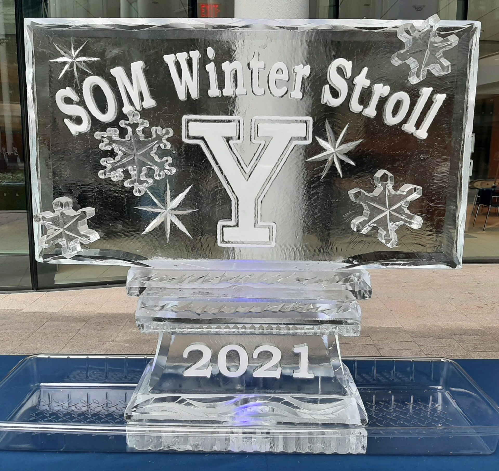 SOM Winter Stroll ice sculpture with a large Y and 2021 base, set in a blue-lit fountain