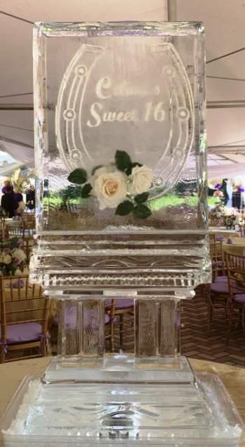 Clear ice sculpture with flowers and engraved “Sauc 16” at a banquet table