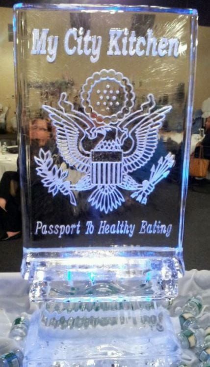 Clear engraved glass plaque reading “My City Kitchen” with “Passport & Healthy Eating” on a stand.