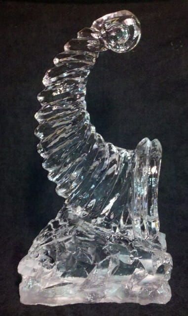 Clear glass abstract sculpture with a curved ribbed form on a rough base against a dark background