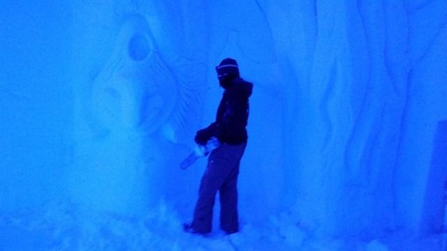 Person standing inside a blue ice cave with carved icy walls
