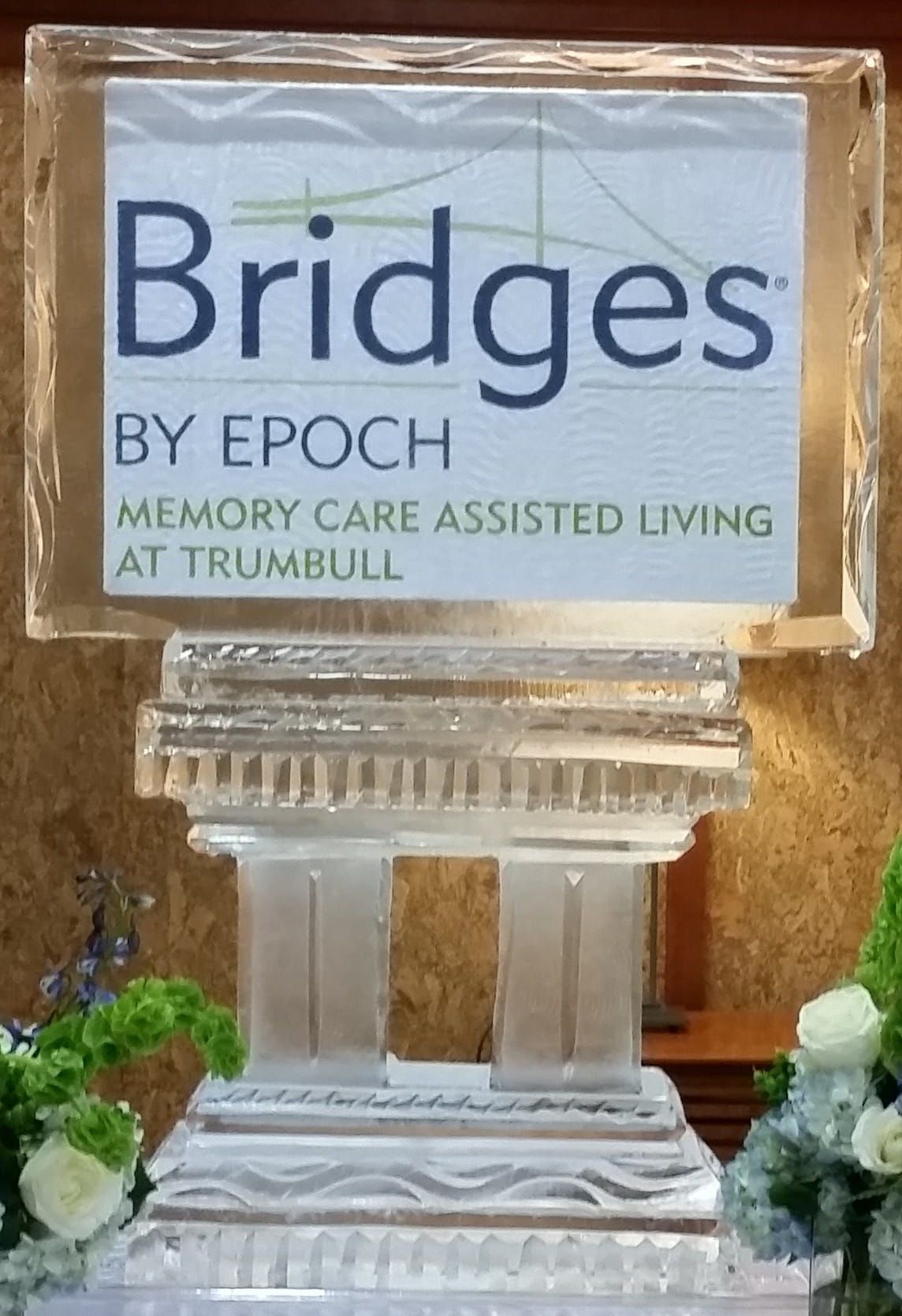 Sign for “Bridges by Epoch” memory care assisted living at Trumbull on a decorative clear stand