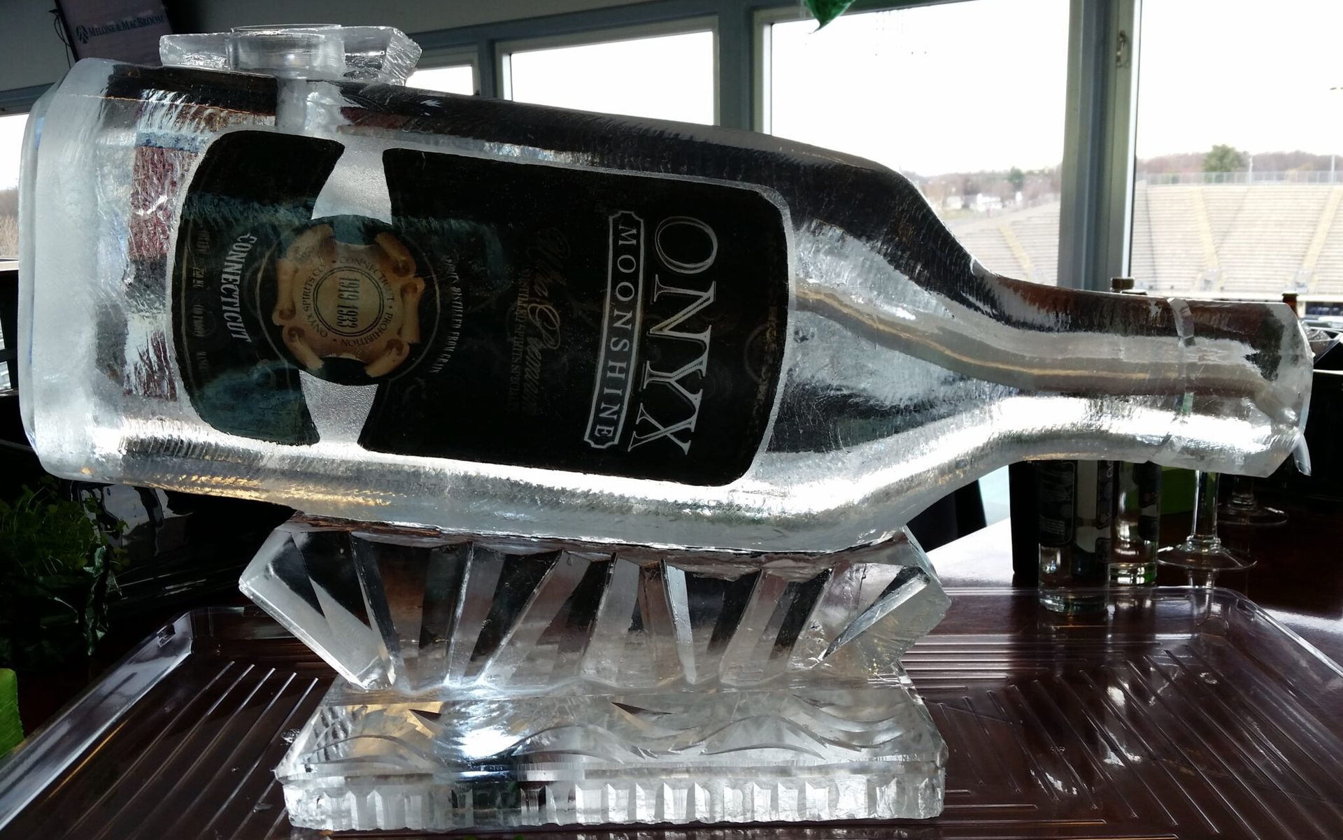 Upside-down glass liquor bottle in an ice bucket on a wooden table, with windows in the background