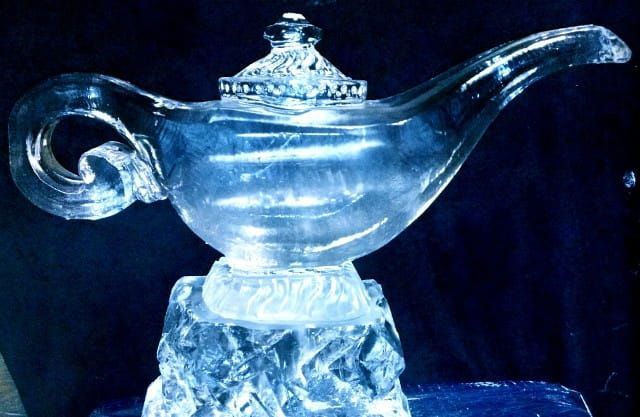 Blue glass genie lamp with a curved spout and ornate handle on a dark background