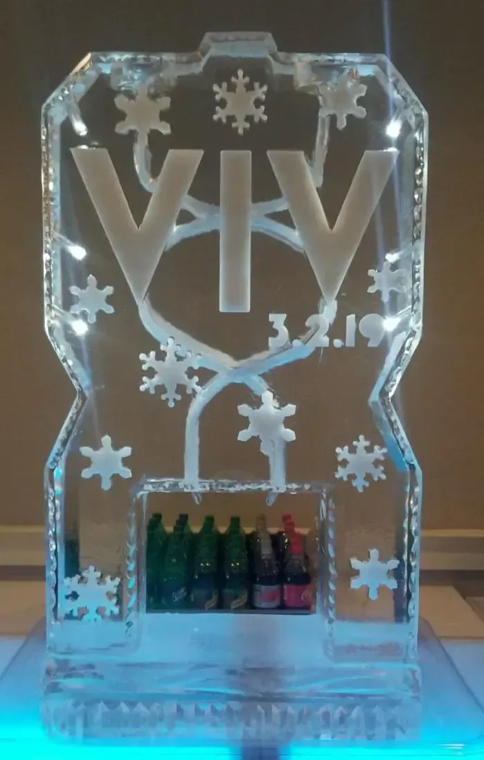 Transparent “VIV” ice sculpture with snowflake cutouts and colorful bottle display at the base