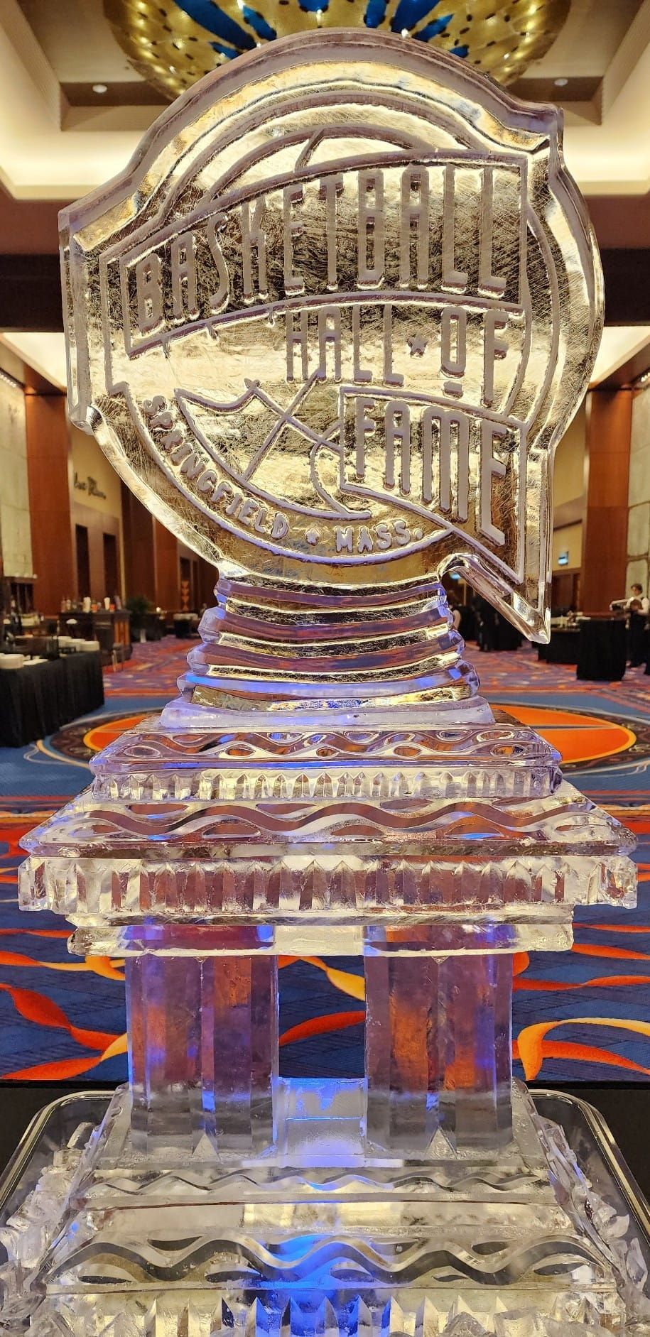 Clear crystal trophy on a table in a banquet hall, lit with blue and warm reflections
