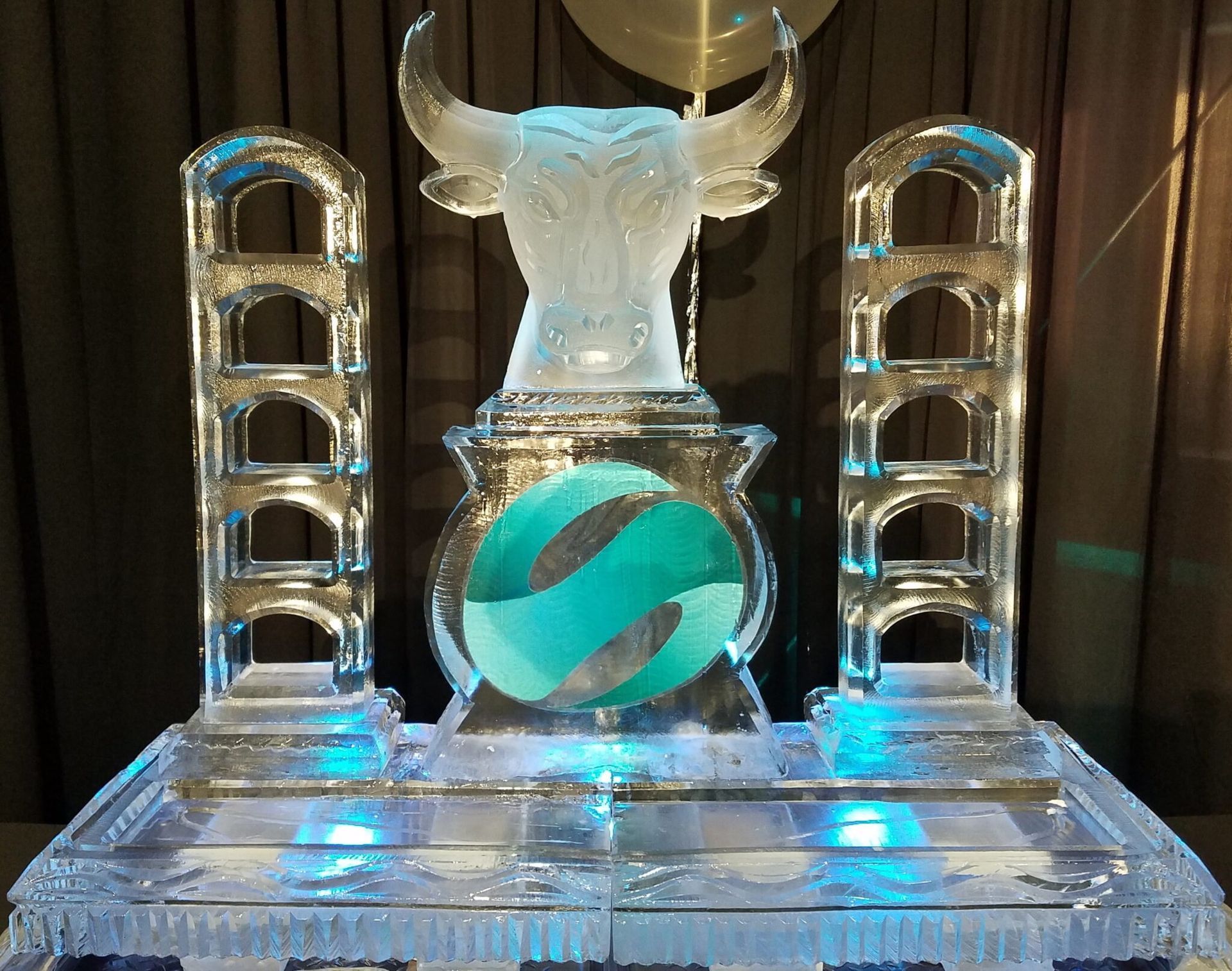 Transparent ice sculpture with a teal sphere centerpiece on a lit display table