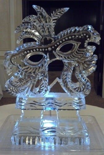 Silver ornate masquerade mask on a clear glass stand with blue light underneath