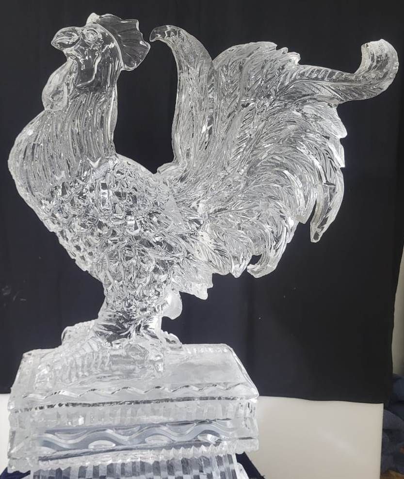 Clear glass rooster figurine on a decorative base against a dark background