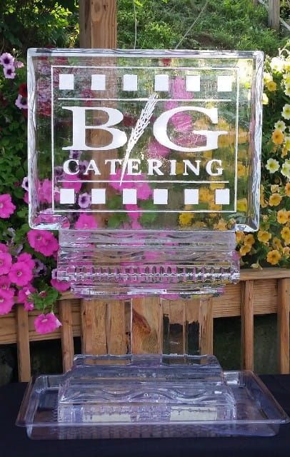 Clear acrylic award with “B/G Catering” logo in front of flowers and wooden railing