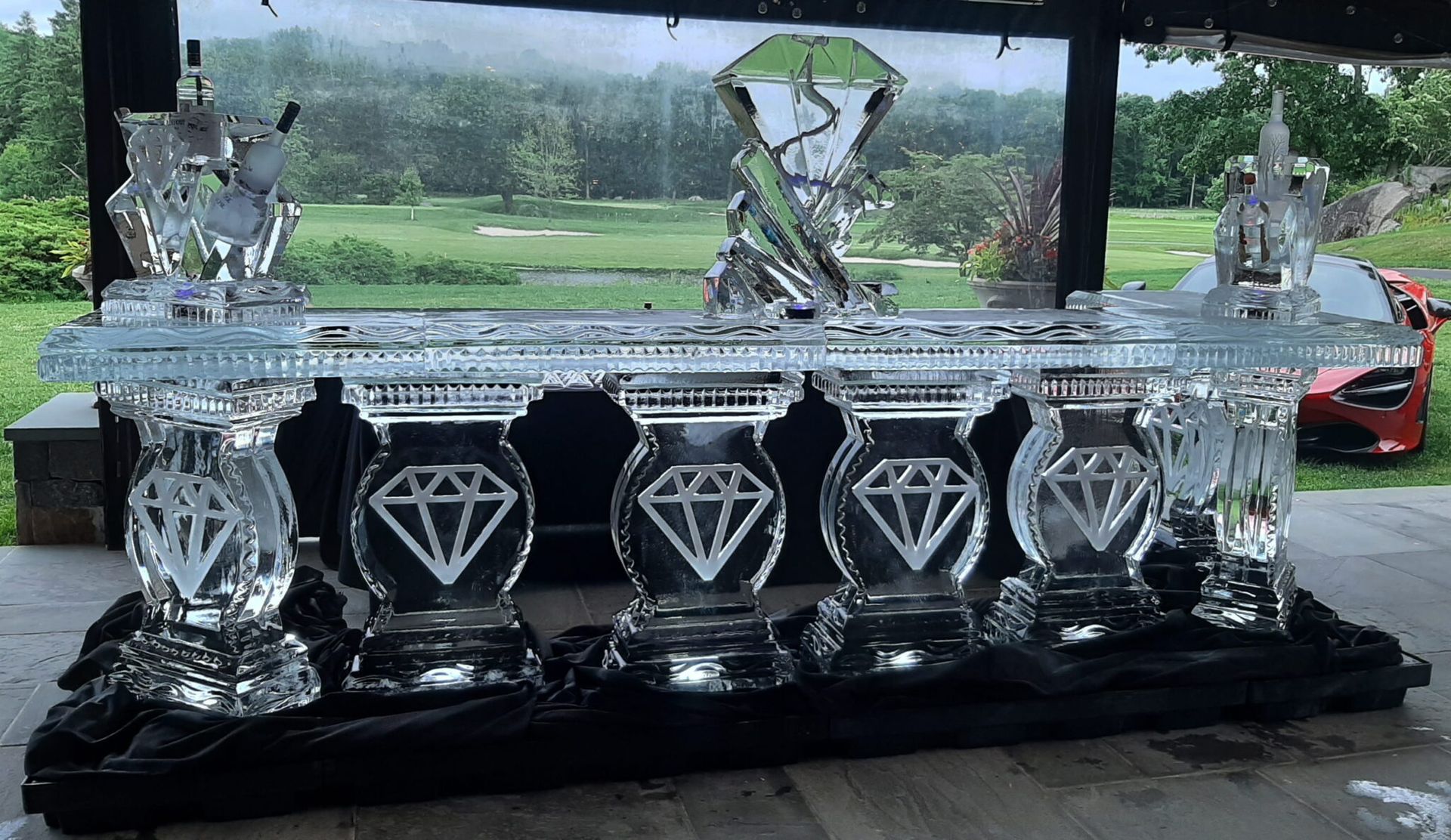 Crystal trophy with diamond emblems displayed on a black base, outdoors under a pavilion.