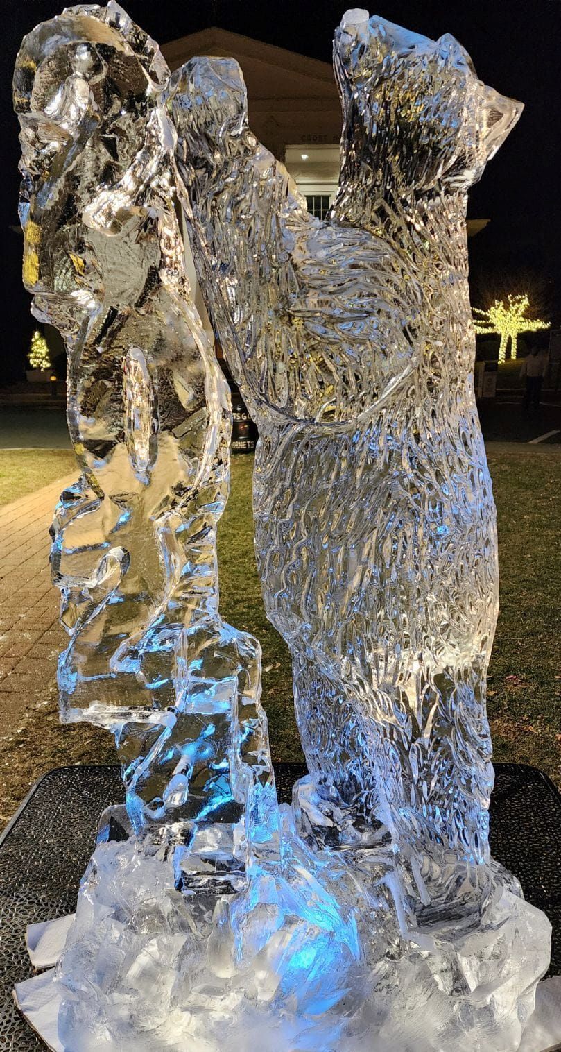 Transparent ice sculpture of two people standing together outdoors at night, lit blue from below