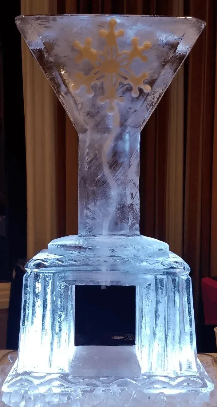Ice sculpture of a funnel atop a blocky base, glowing white against dark curtains.