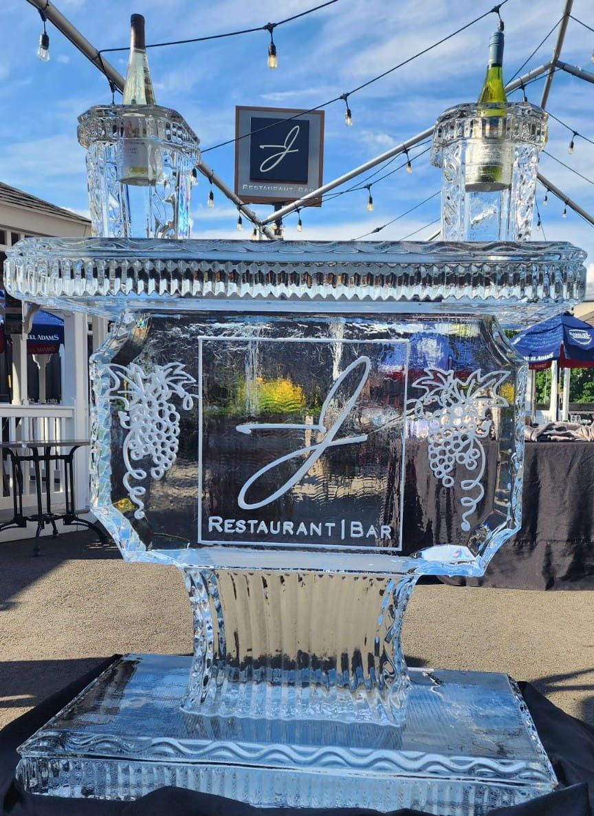 Clear ice sculpture with logo and “Restaurant Bar,” outdoors under string lights at a waterfront venue