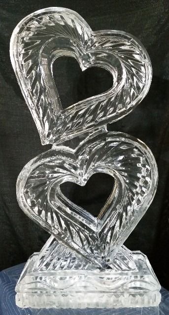 Two stacked clear glass heart sculptures on a base against a dark background
