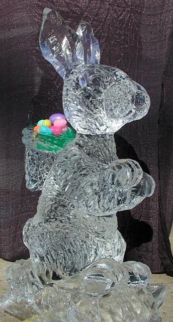 Clear glass rabbit sculpture holding a colorful Easter basket, with crystal-like ears and paws