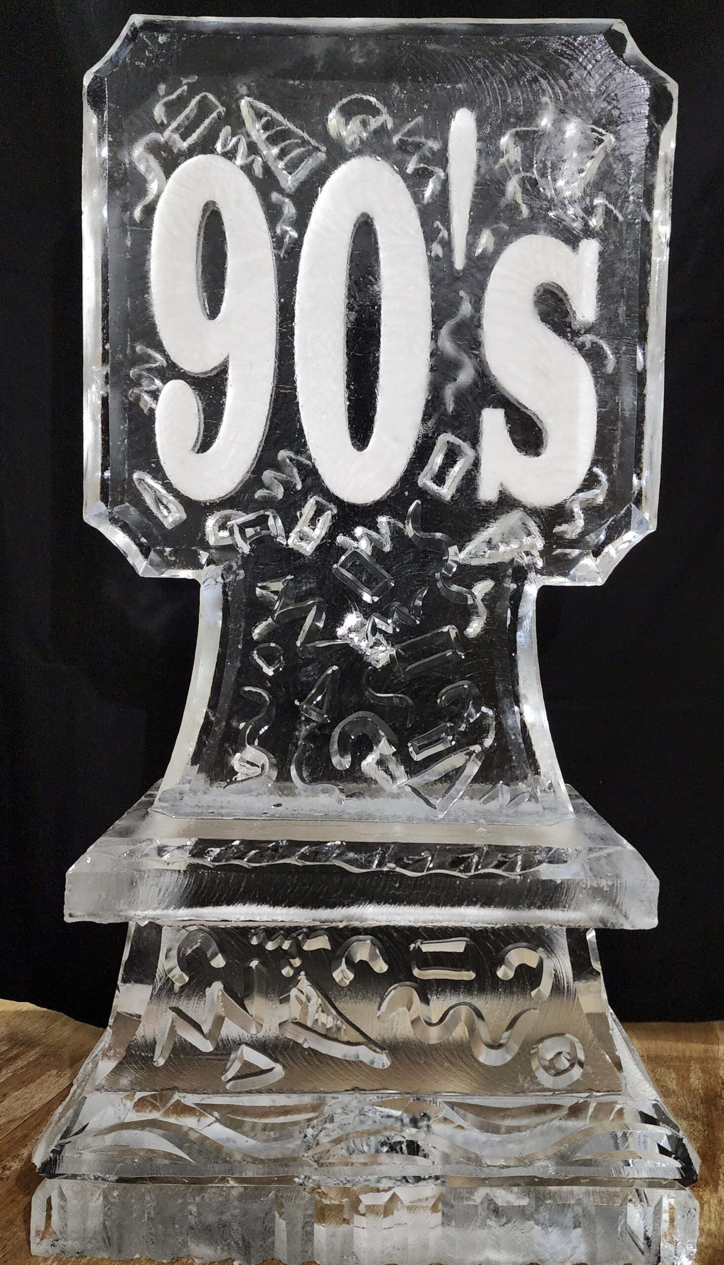 Clear ice sculpture engraved with “90s” on a black background