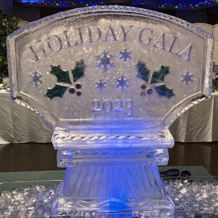Ice sculpture reading “Holiday Gala 2023” with blue lighting and holly decorations