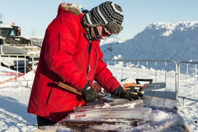 Person in red coat carving ice outdoors with snowy mountains in the background