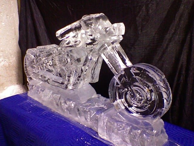 Clear glass motorcycle sculpture on a blue cloth against a dark background