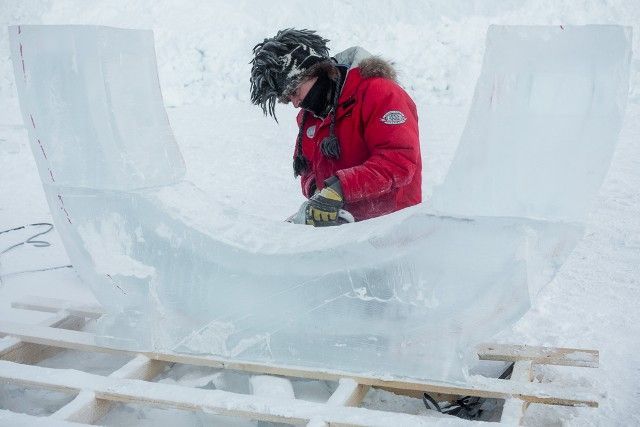 Person in a red jacket carving an ice block with a chainsaw in a snowy outdoor setting