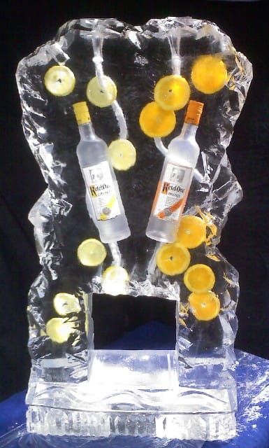 Clear trophy with floating orange and yellow discs, and two bottles inside on a blue base