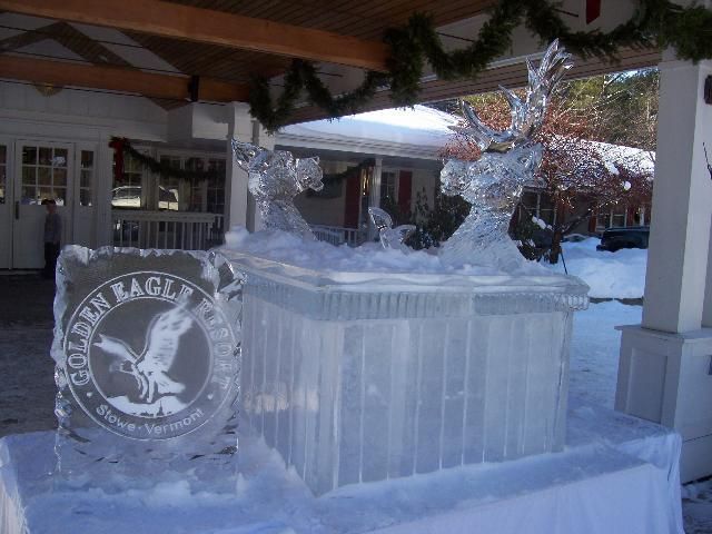 Ice sculpture on a pedestal at an outdoor event, with a circular logo carved into the ice