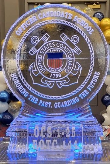 Glowing acrylic U.S. Coast Guard logo display at Officer Candidate School event, in blue and white lights