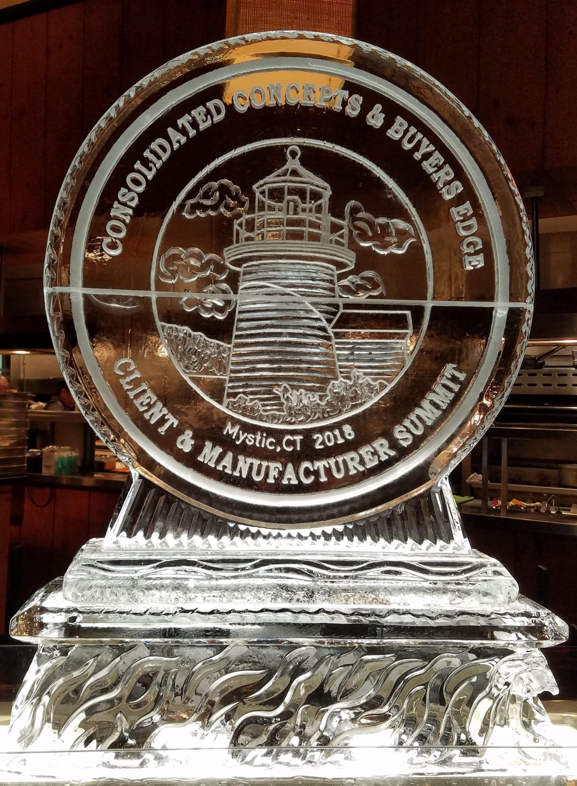 Clear glass trophy plaque with engraved lighthouse design and circular text on a wooden background