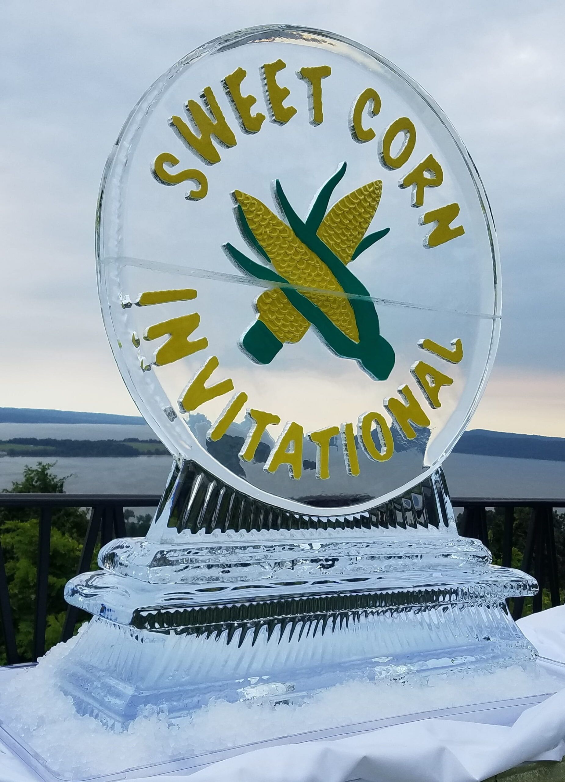 Sweet Corn Invitational ice sculpture with corn and gold lettering on a snowy pedestal outdoors