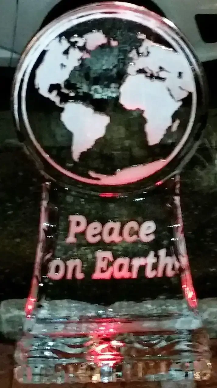 A glass globe with “Peace on Earth” lit in pink, set on a clear base.