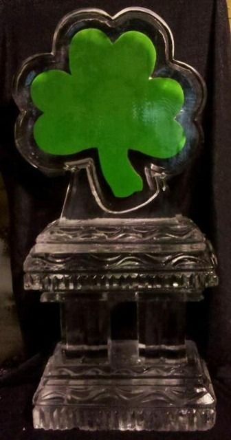 Green shamrock-shaped trophy on a clear pedestal against a dark background