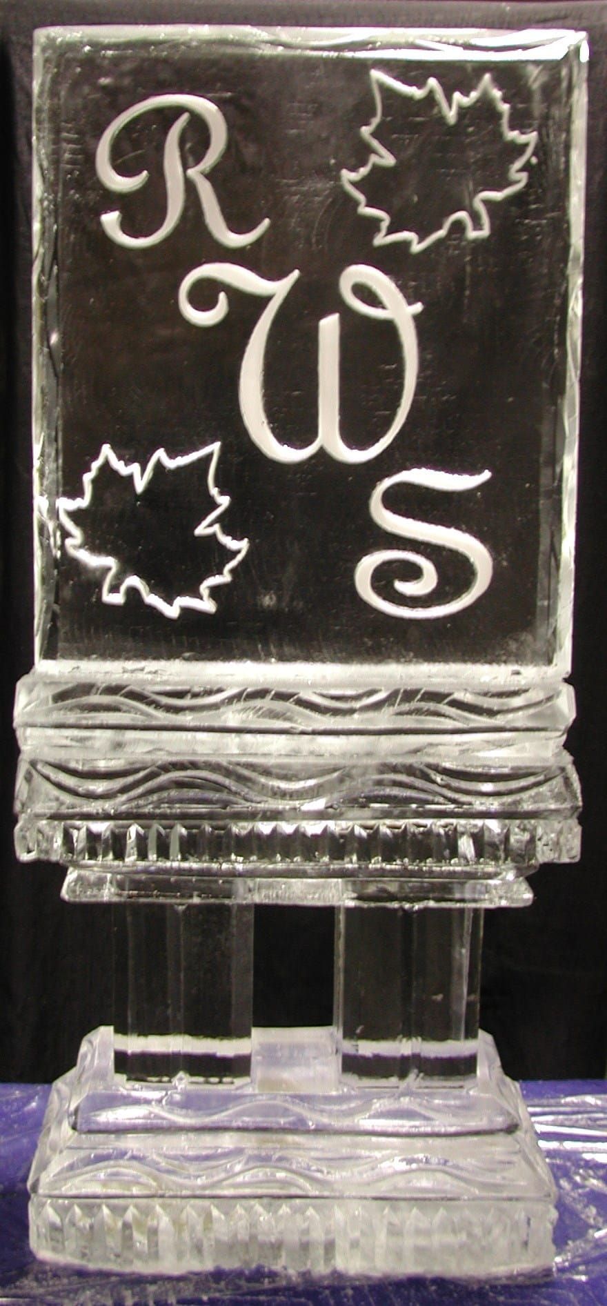 Clear glass award engraved with stylized initials and maple leaf designs on a pedestal base