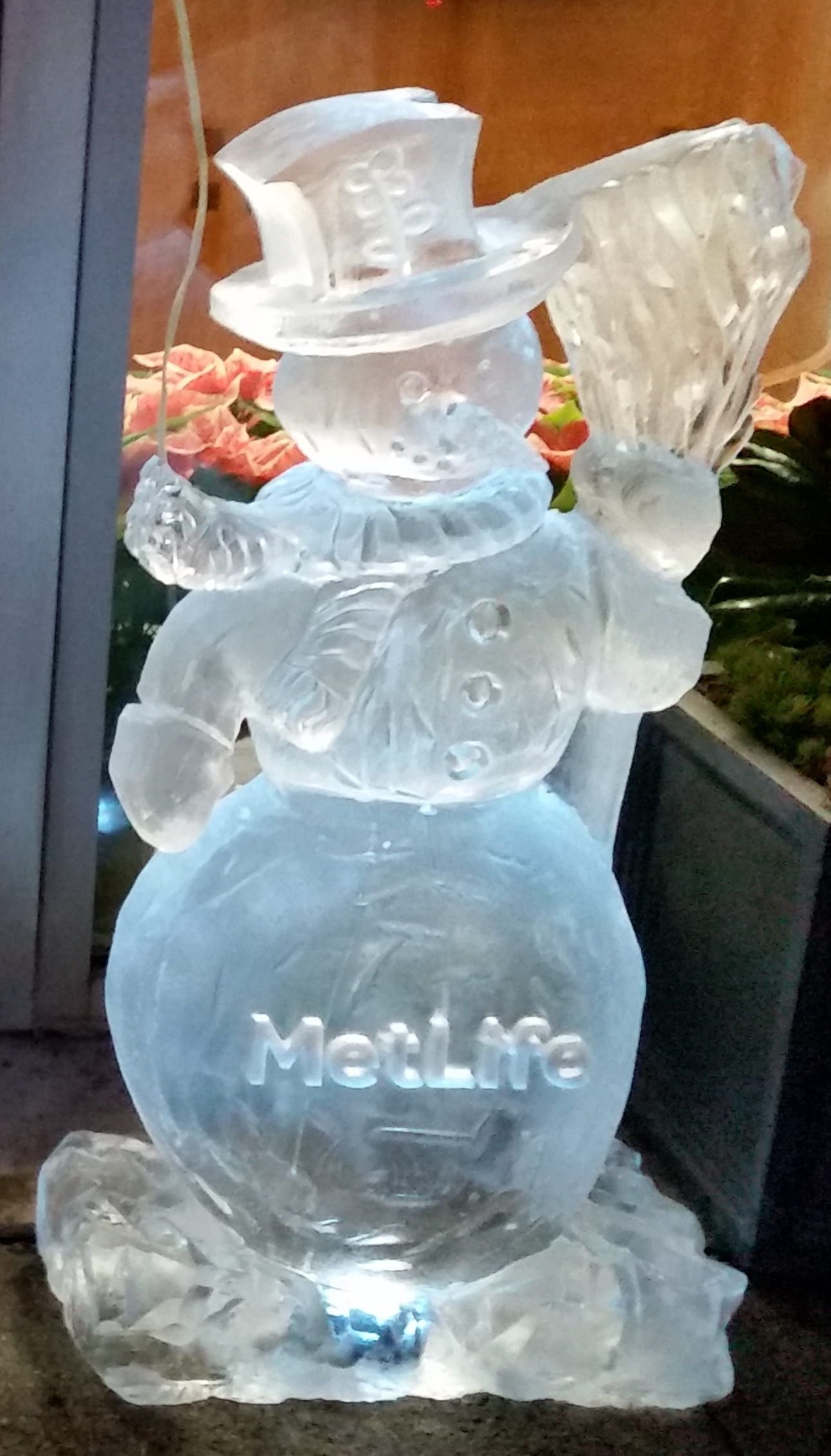 Clear glass snowman sculpture with top hat and scarf, lit from below on a tabletop