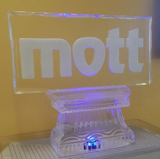 Clear acrylic sign reading “mott” on a glowing purple-lit stand against a yellow background