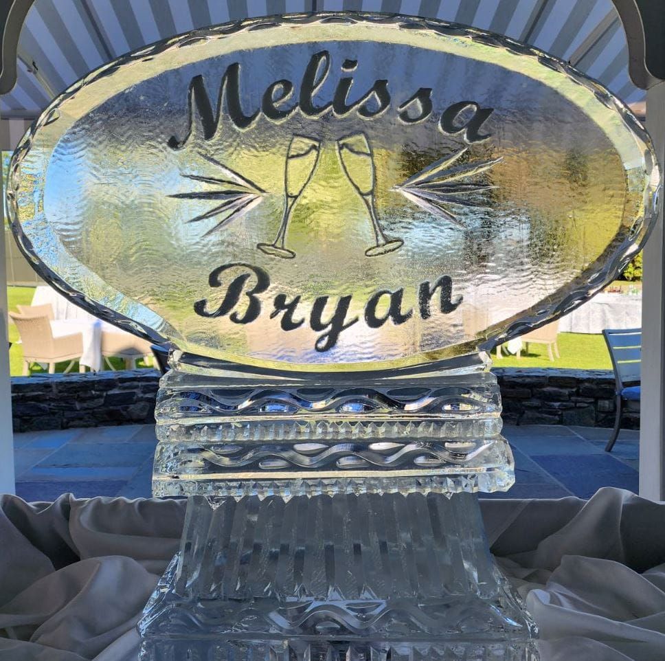 Personalized glass cake topper reading “Melissa Bryan” on a sparkling gold oval plaque