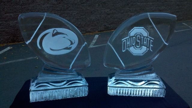 Two clear glass trophies on a dark surface, one with a Penn State logo and one with an Ohio State logo.