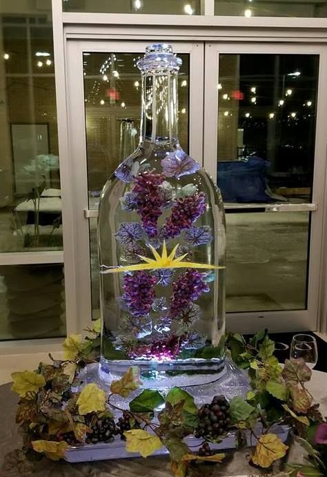 Decorative glass bottle centerpiece with purple flowers and lights on a leaf-covered table indoors