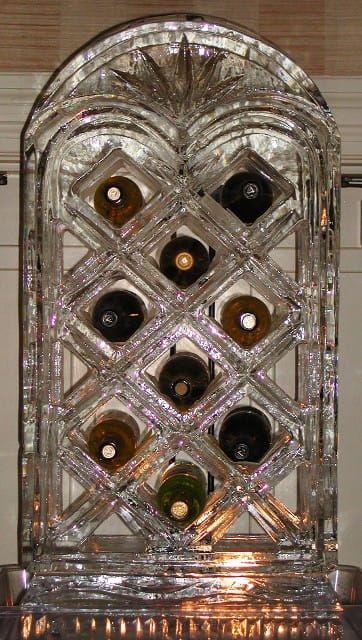Crystal wine rack with several wine bottles displayed against a brick wall