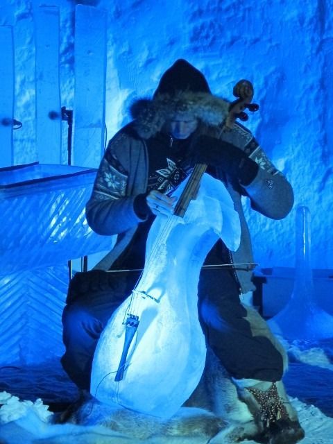 Person in winter gear carving a large ice sculpture in a blue-lit ice room