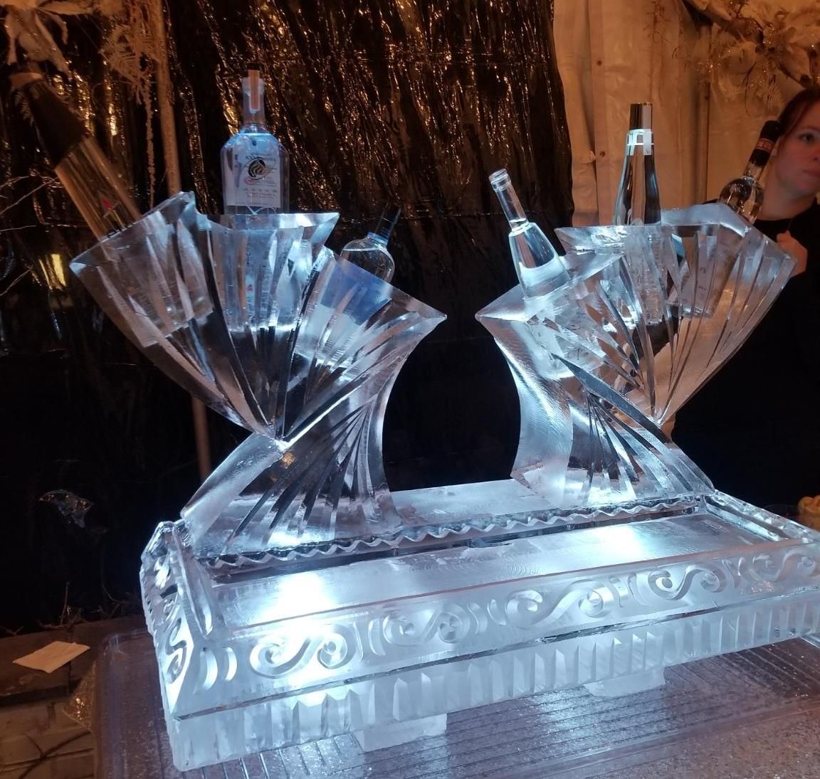 Ice sculpture of two swan-like figures on a reflective base, lit in blue and white.