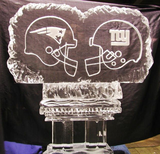 Football helmets with Patriots and Giants logos engraved in clear glass on a crystal stand
