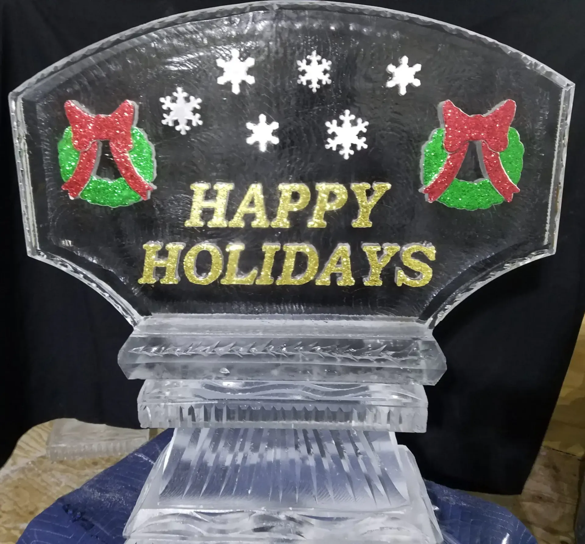 Clear acrylic “Happy Holidays” sign with red and green accents and white snowflakes on a black background