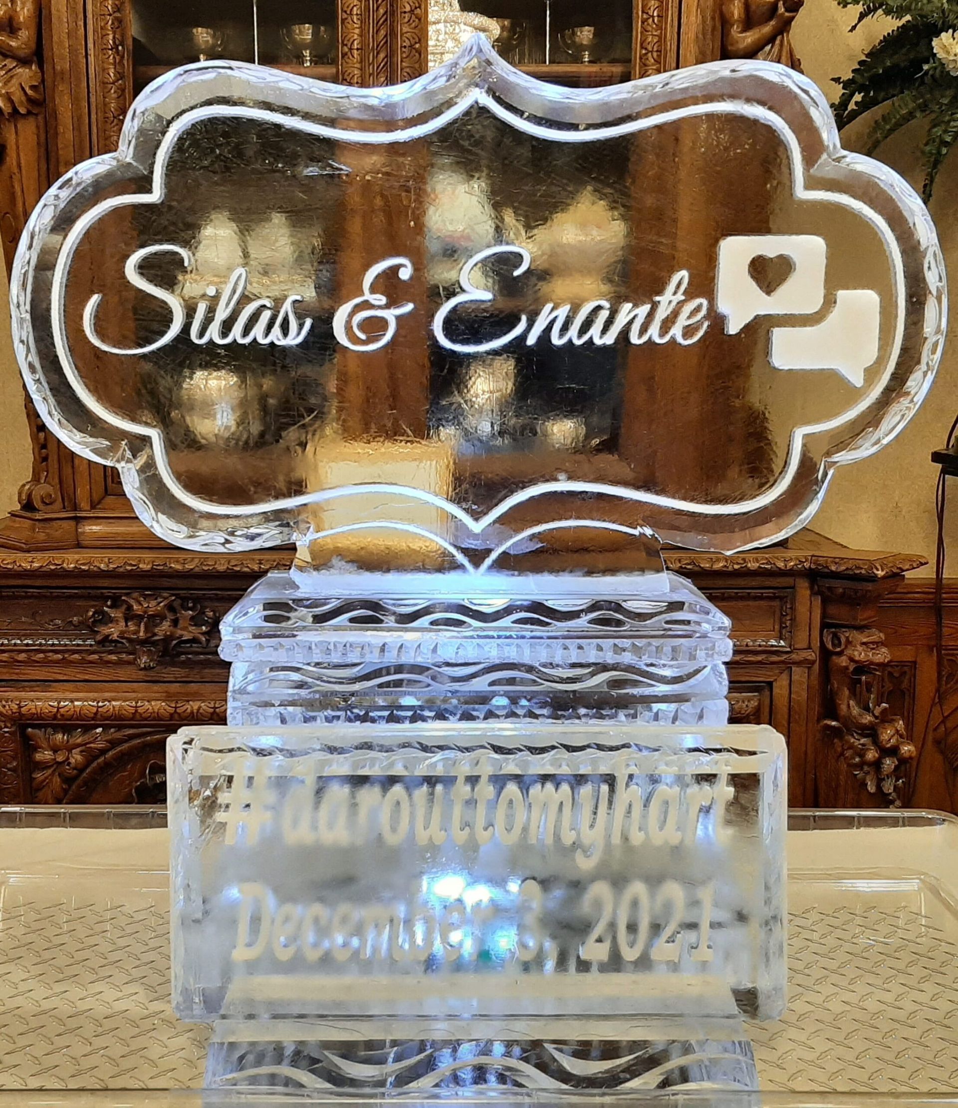 Clear acrylic sign reading “Silas & Charite” with a camera icon above a frosted base, in a decorative setting
