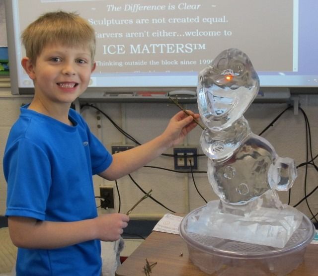 Boy in blue shirt beside a clear ice sculpture in a classroom demonstration