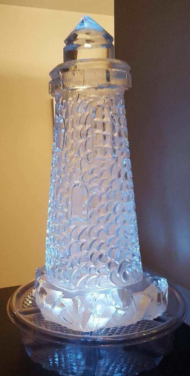 Clear glass lighthouse-shaped decorative candle holder on a glass base, lit from within with a blue glow
