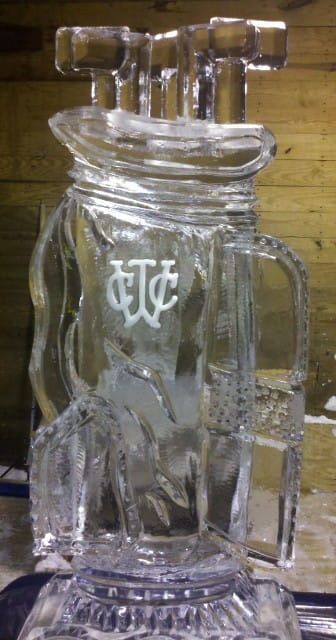 Clear glass beer stein with handle and etched logo, viewed from the front on a wooden surface